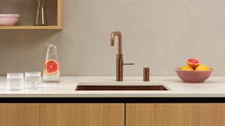 copper boiling water tap on white worktops with water jug and two glasses and fruit bowl