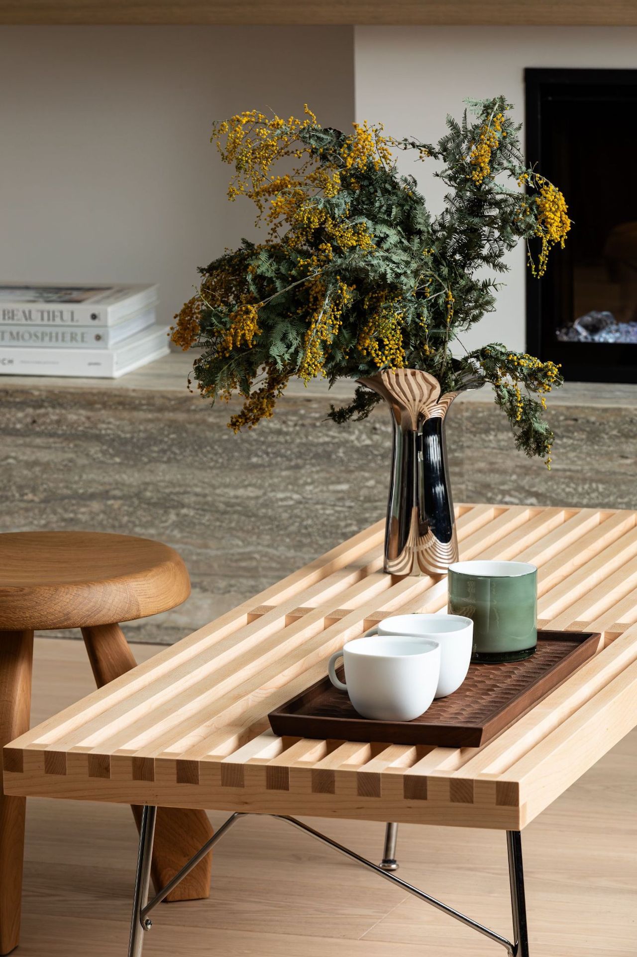 A close up view of the coffee table in the living space, with some coffee cups on top, as well as a vase of flowers and a view of a wooden stool behind.