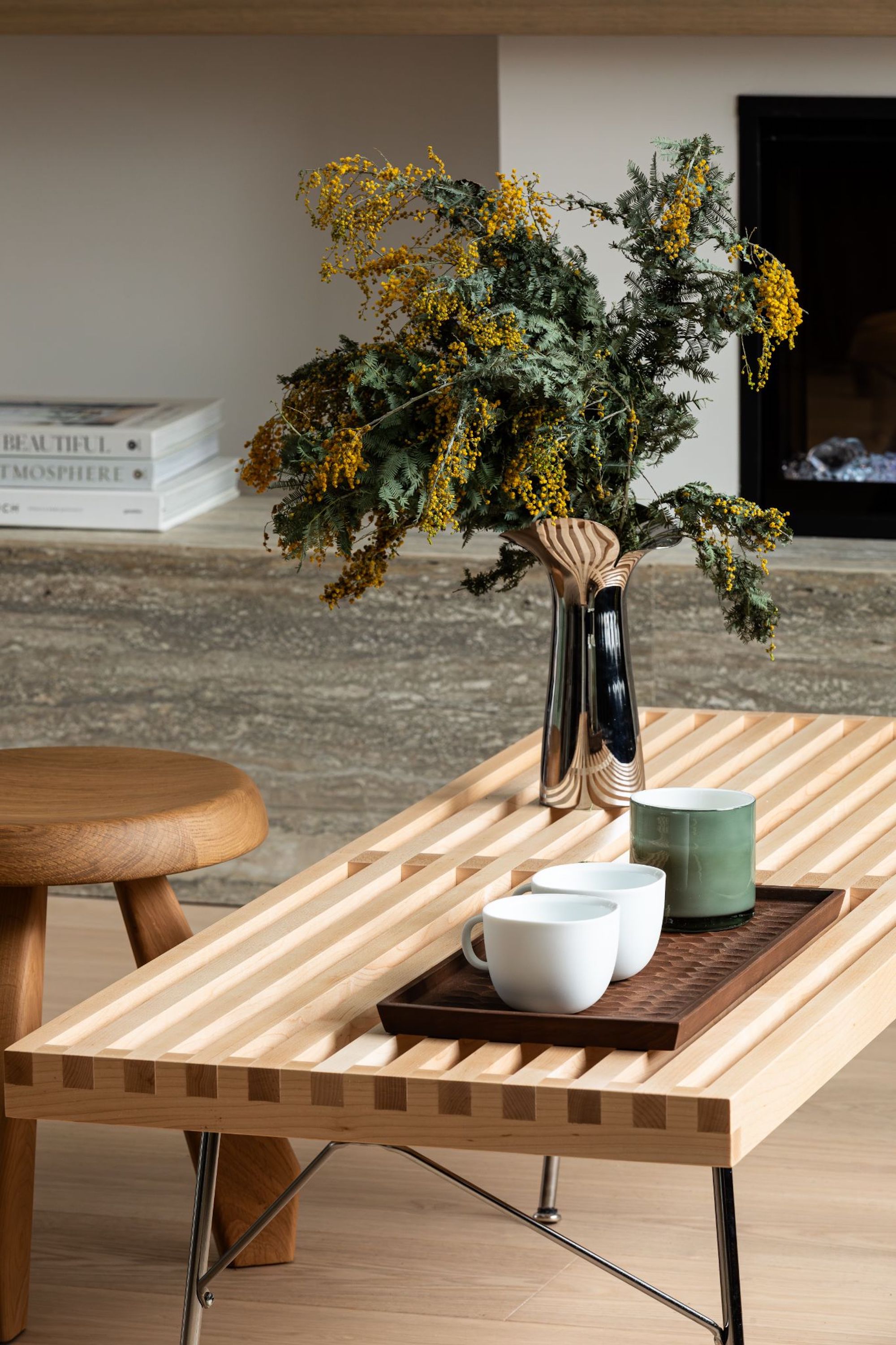 A close up view of the coffee table in the living space, with some coffee cups on top, as well as a vase of flowers and a view of a wooden stool behind.
