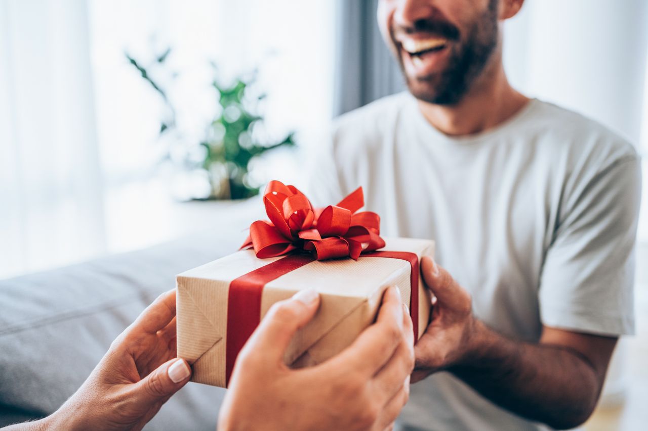 A smiling man receiving a gift wrapped in brown paper and decorated with a red bow. 