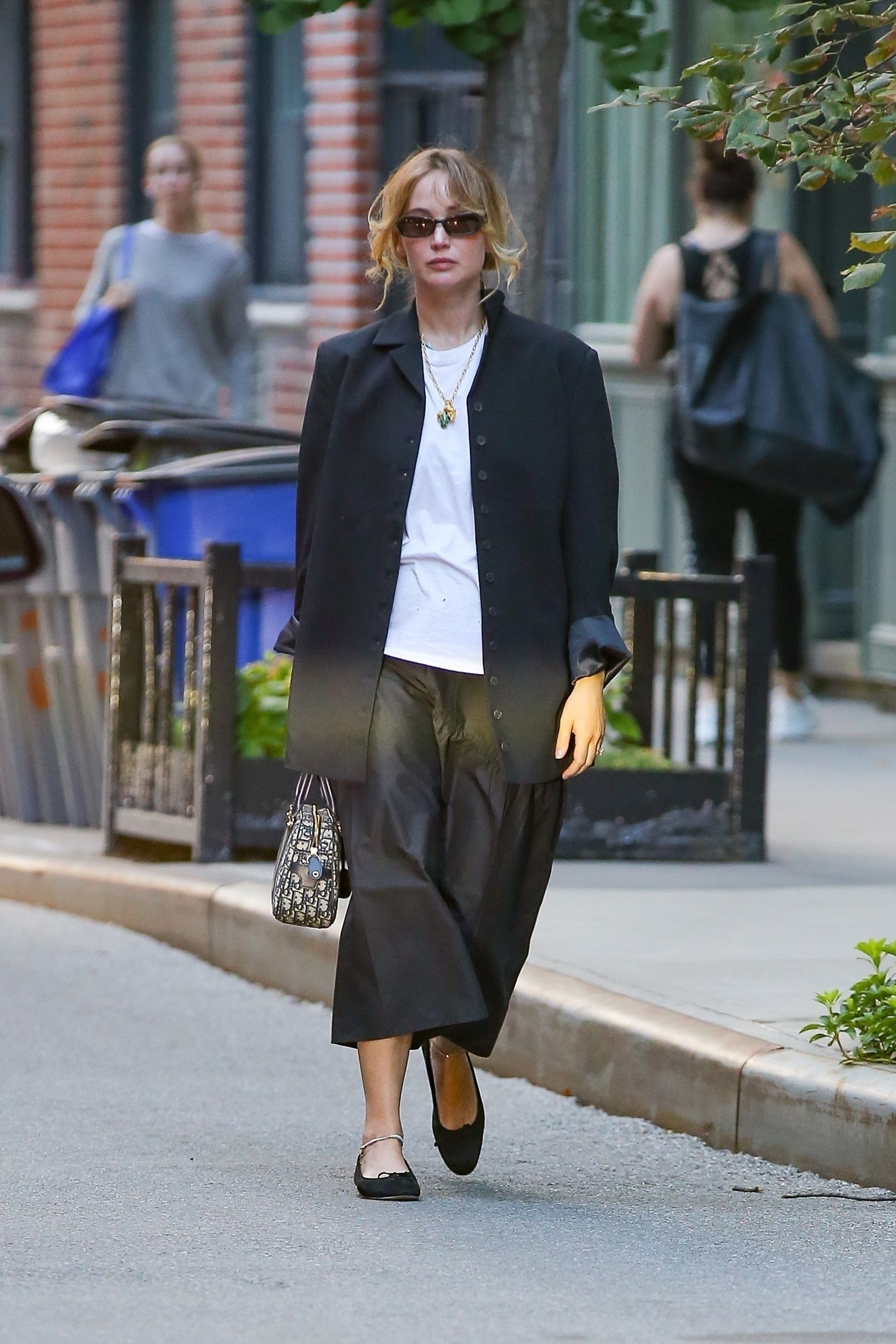 Jennifer Lawrence walks through New York wearing a black midiskirt with black ballet flats and a black single breasted jacket.