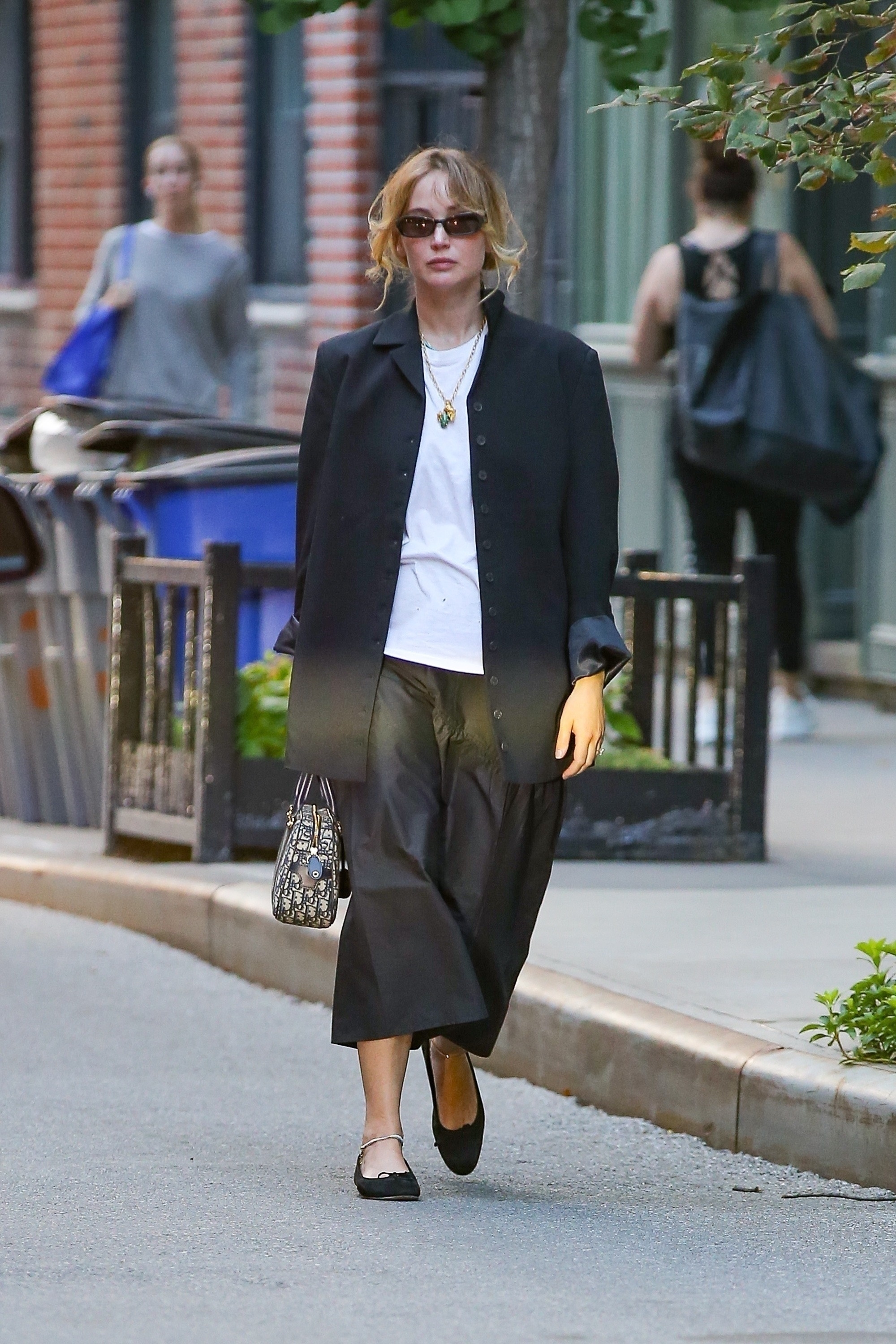 Jennifer Lawrence walks through New York wearing a black midiskirt with black ballet flats and a black single breasted jacket.