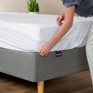 A hand pulling on the Purple Mattress Protector.