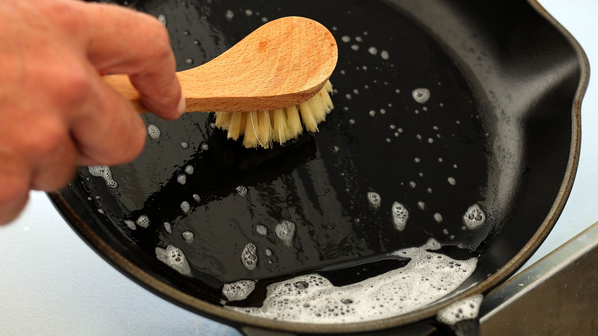 Cast iron skillet being cleaned with warm soapy water and a brush