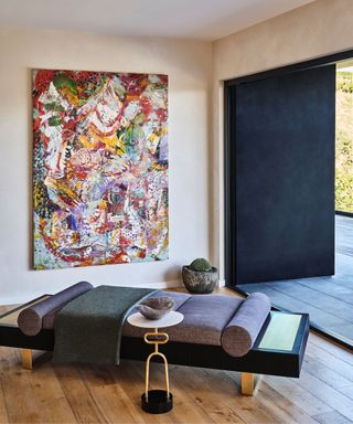 A chaise with a side table and large piece of art in a neutral living room