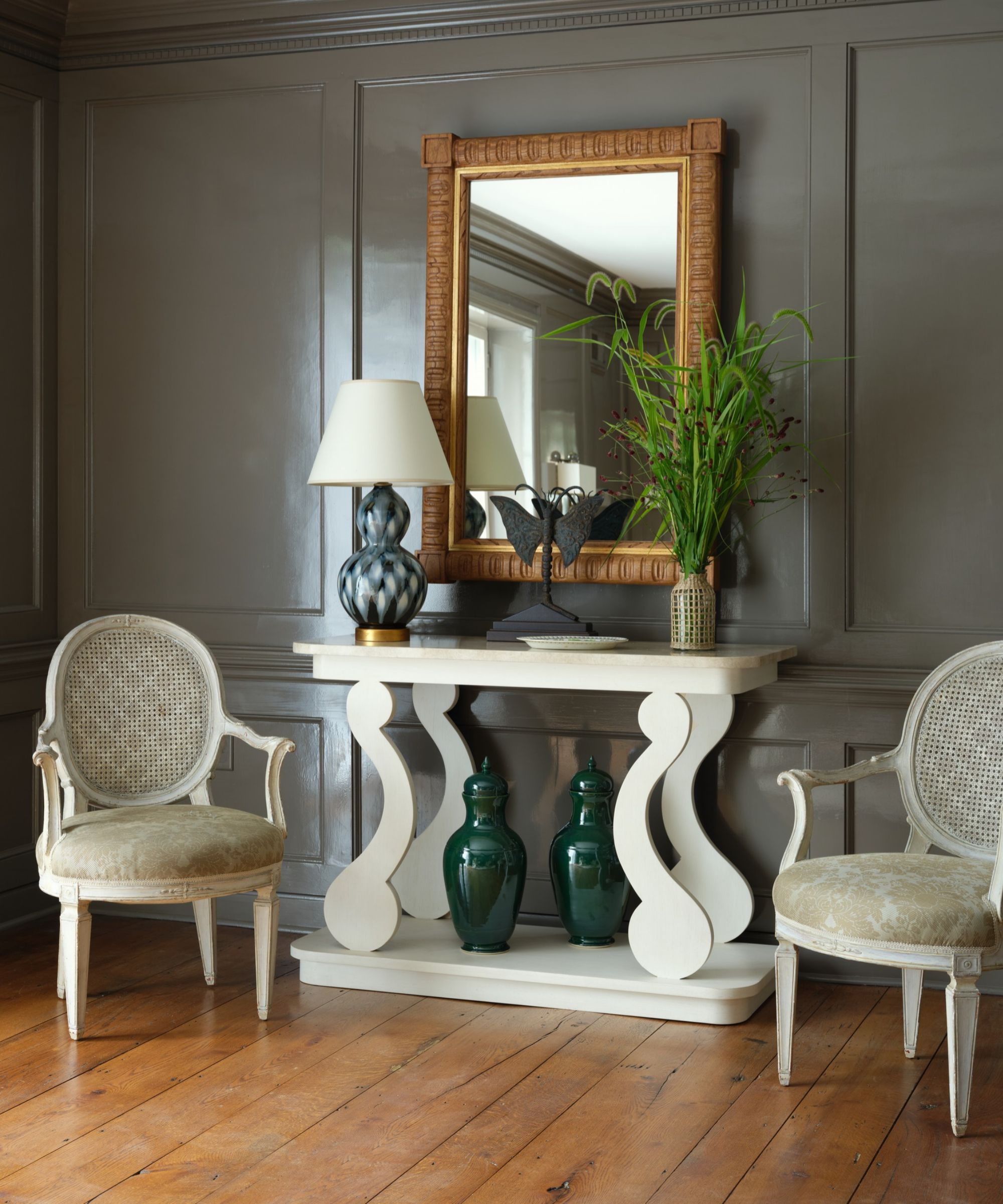 Console table with mirror above, lamp on and armchairs either side
