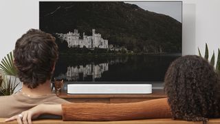 A couple are watching a TV with the Sonos Beam Gen 2 soundbar underneath it