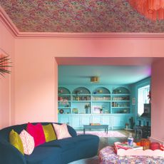 A pink-painted living room with a blue curved sofa and a floral-print wallpapered ceiling