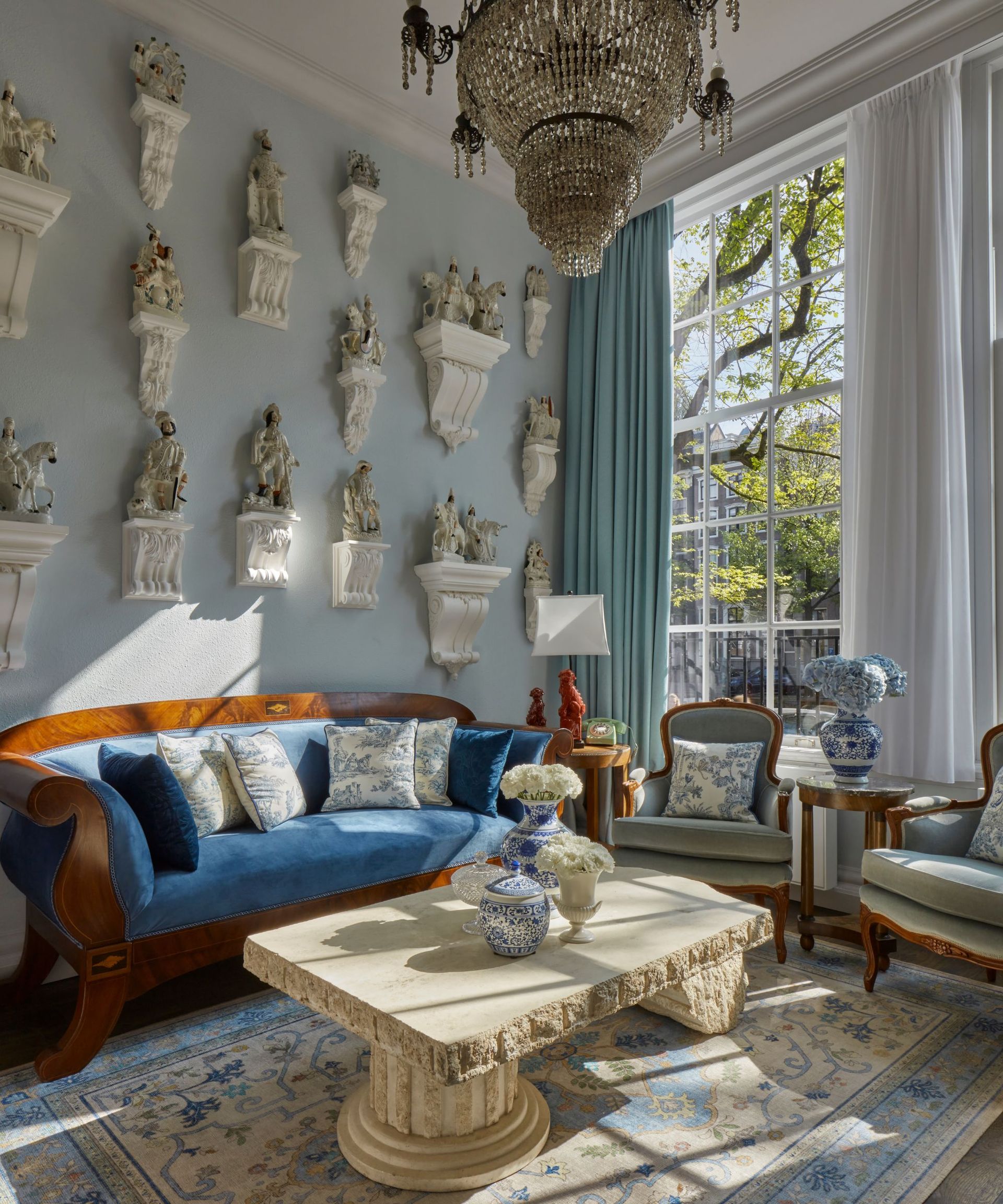 blue hotel living room area filled with a large glass chandelier, antique furniture and a wall of statues
