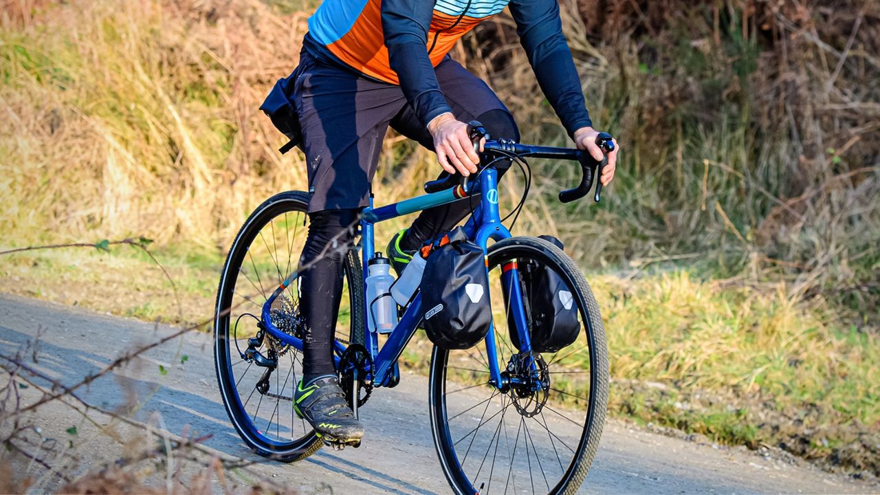 Islabike adult Luath ridden by a male rider with front pannier bags on tarmac with grass at the side of the road, 