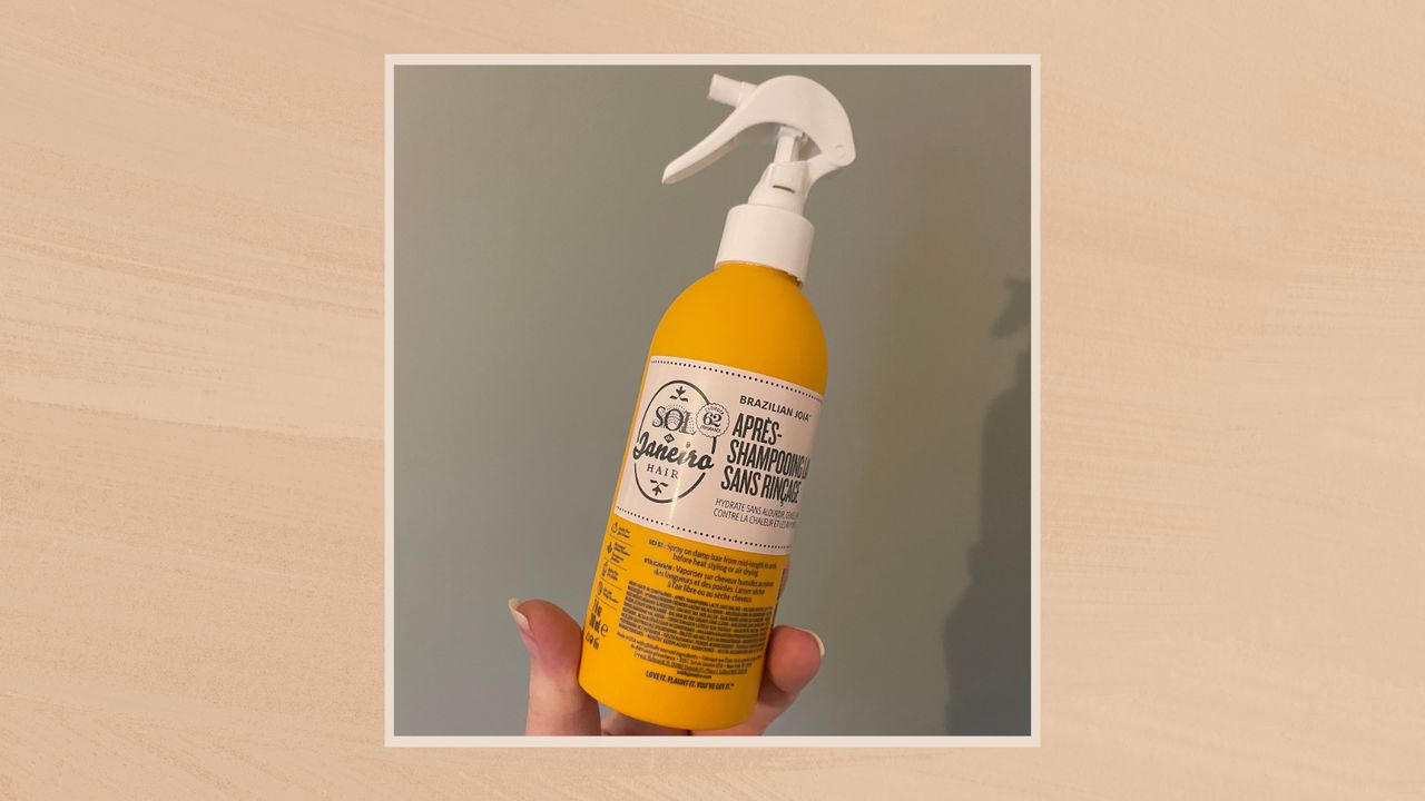 Image showing a handheld view of the Sol de Janeiro Brazilian Joia Milky Leave-In Conditioner, in a taupe frame against a warm beige watercolour style background