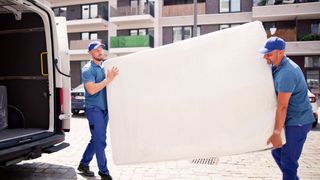Two delivery men take a mattress that is being returned and carry it to a white van