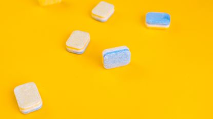 White and blue dishwasher tablets on bright yellow background