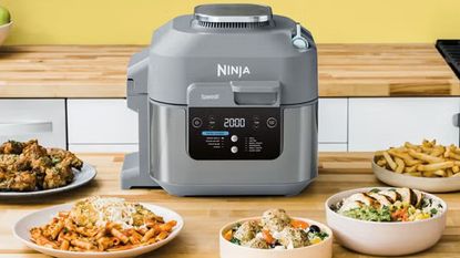 Ninja Speedi Rapid Cooker and Air Fryer on a kitchen counter, surrounded by plates of air-fried food.