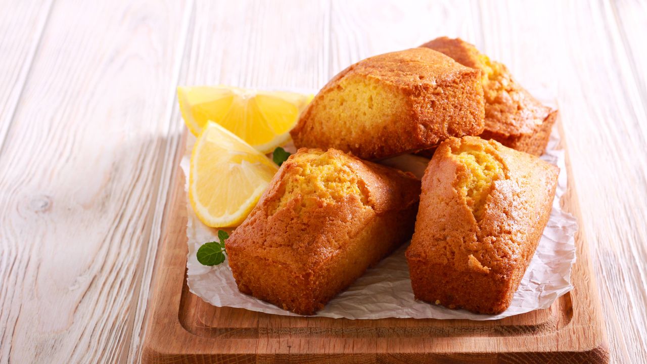 Mini lemon cakes stacked on a wooden board with fresh wedges of lemon on the side