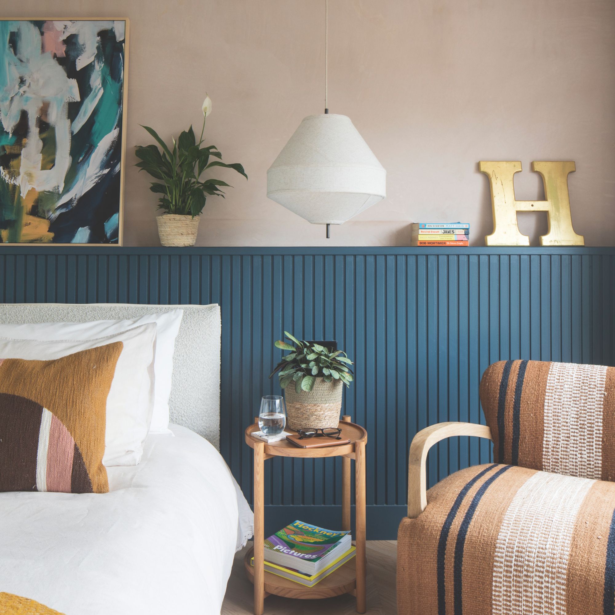 Pink painted bedroom with blue panelling behind the white bed. There's a small round side table and a brown accent chair next to the bed