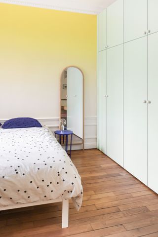 A bedroom with a slim mirror placed next to the bed