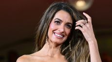 Image of Amal Clooney smiling with hand sweeping through side-part long brunette hair 