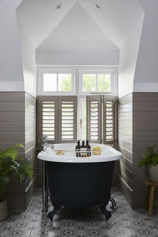 bathroom with roll top bath, brown paneling and cafe shutters