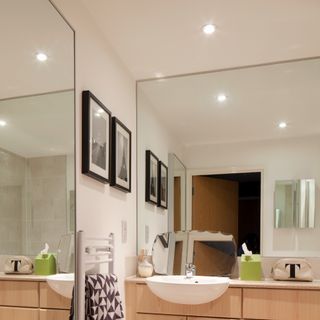 A bathroom with a large mirror and switched on downlights