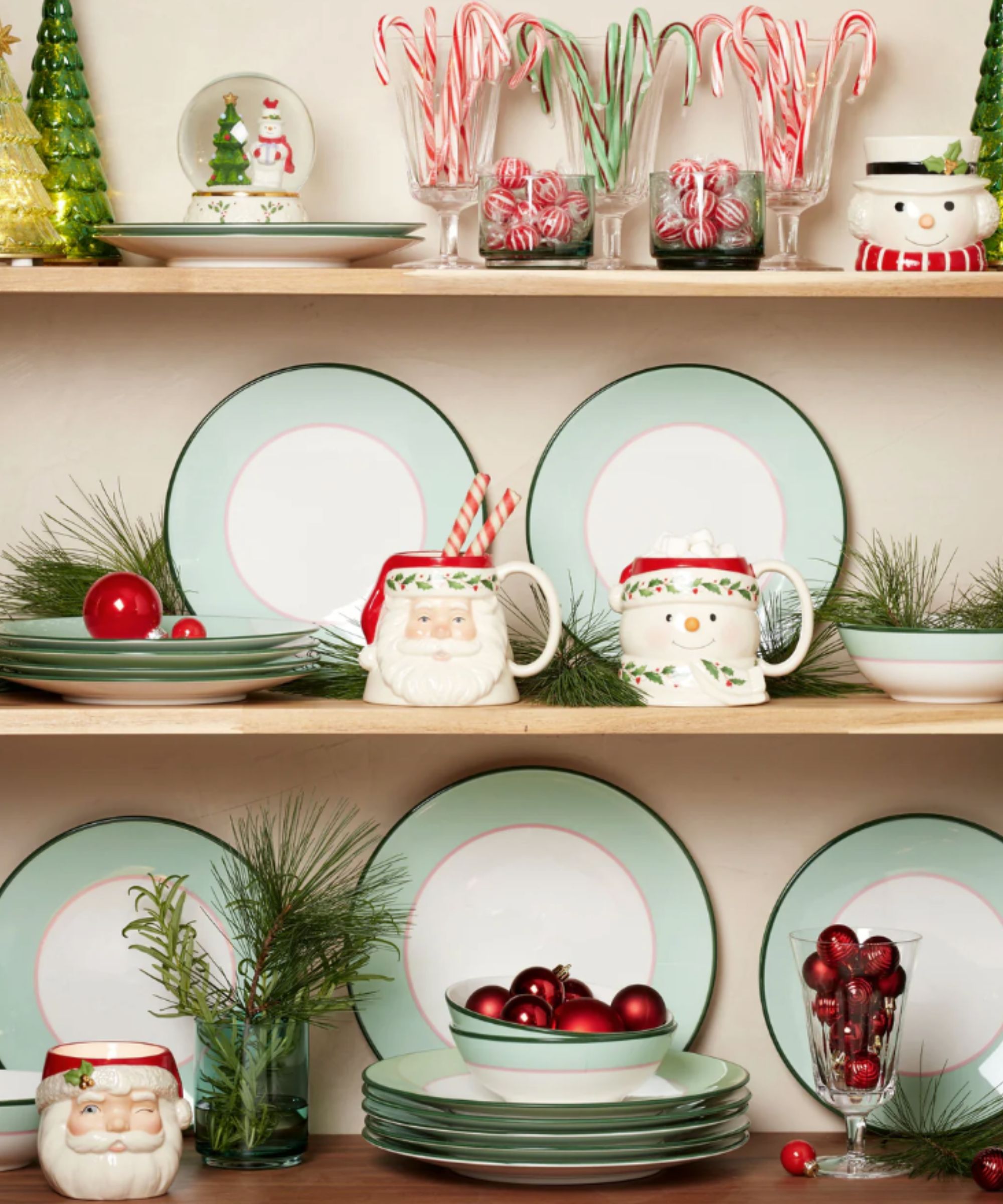 Open cabinet with green and pink plates, santa mugs, candy canes and red baubles