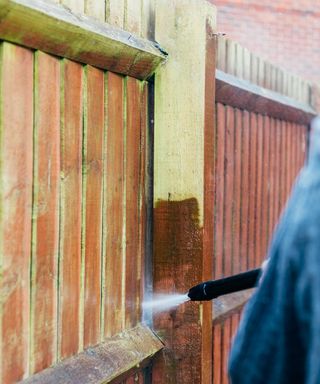 A fence with greenish patches of algae being blasted away with a pressure washer