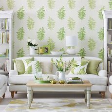 Green printed wallpaper behind a white sofa with green cushions