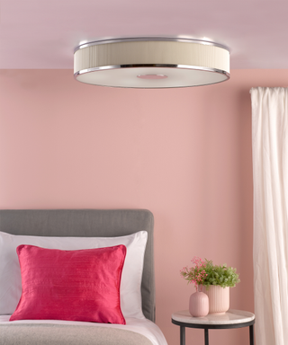 A pink bedroom with a flush ceiling light hung above the bed