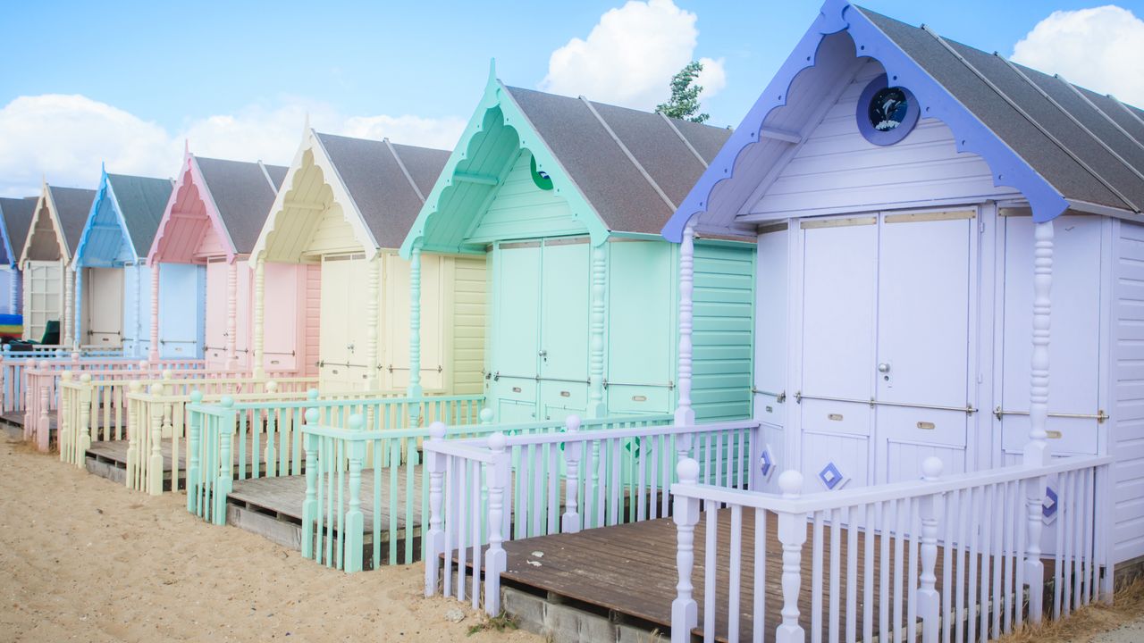 pastel coloured beach huts in a row with sandy beach in front