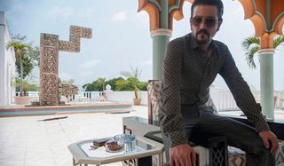 Narcos: Mexico Diego Luna sits on a counter, near a rich looking pool