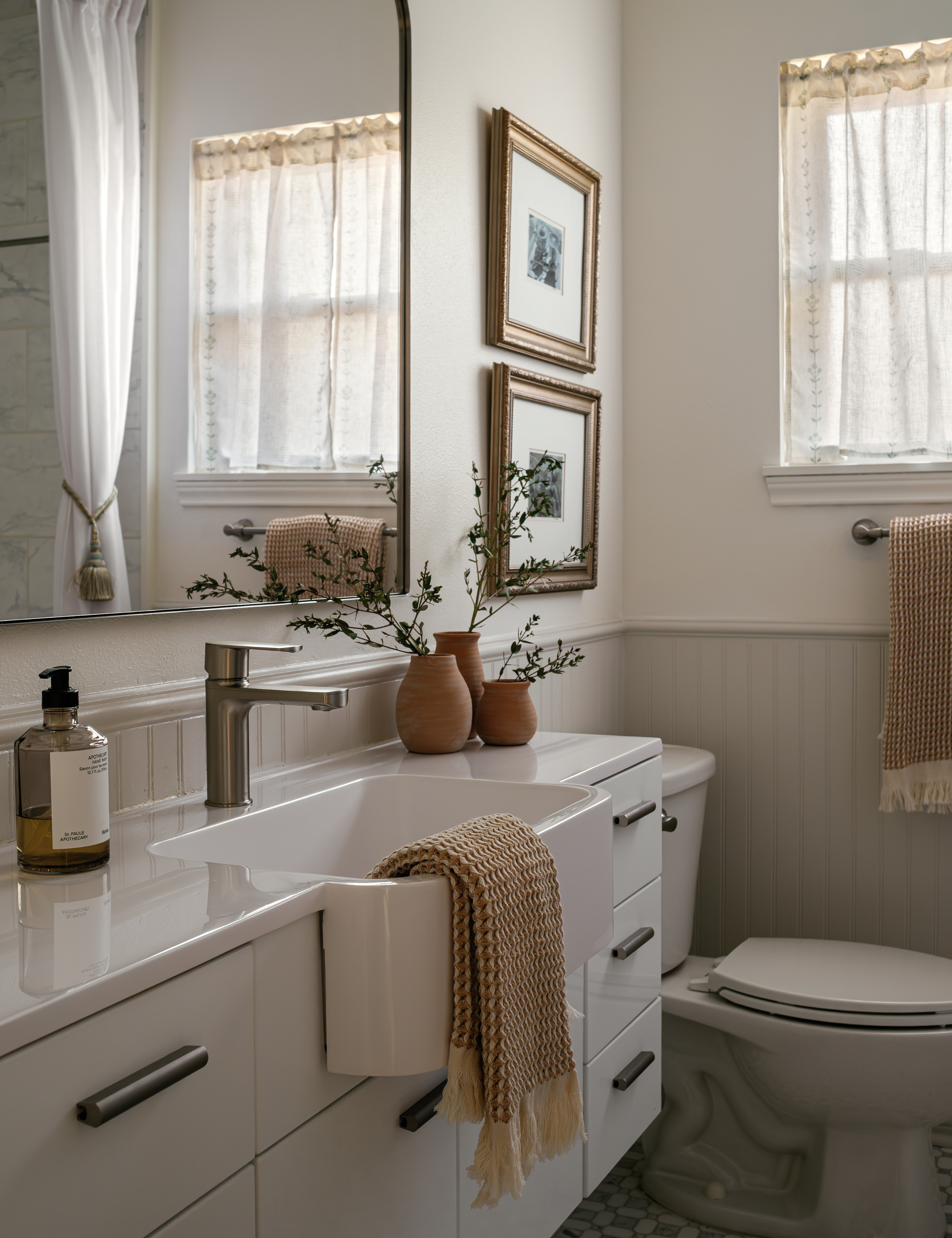 Collected guest bathroom featuring a woven hand towel, tassel curtain ties, and wall art