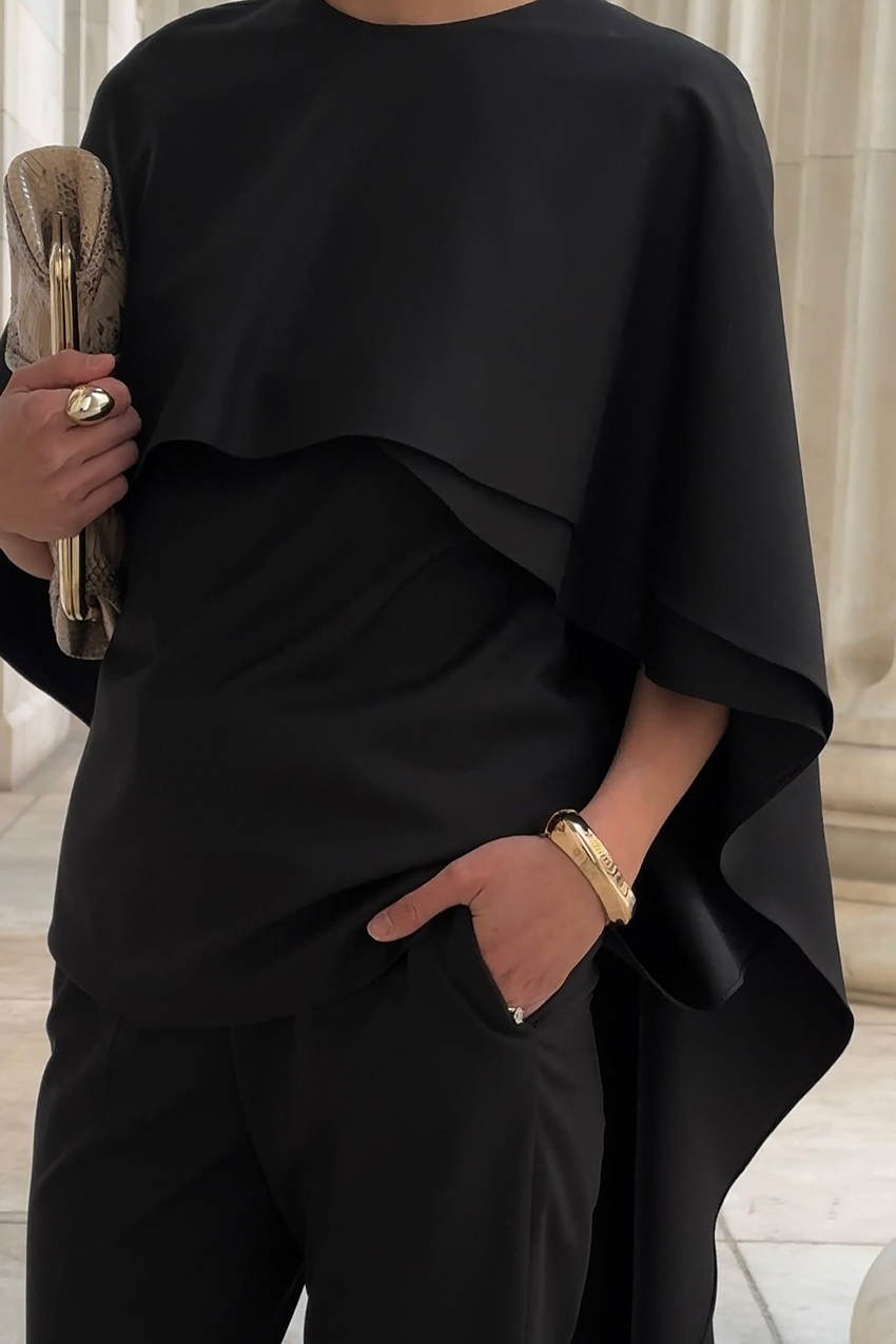a woman wearing a black silk cape and gold jewelry