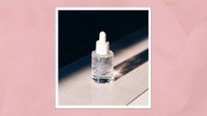 A close up of a glass serum bottle containing a clear liquid, with the sun shining on it creative a silohuette/ in a pink textured template 