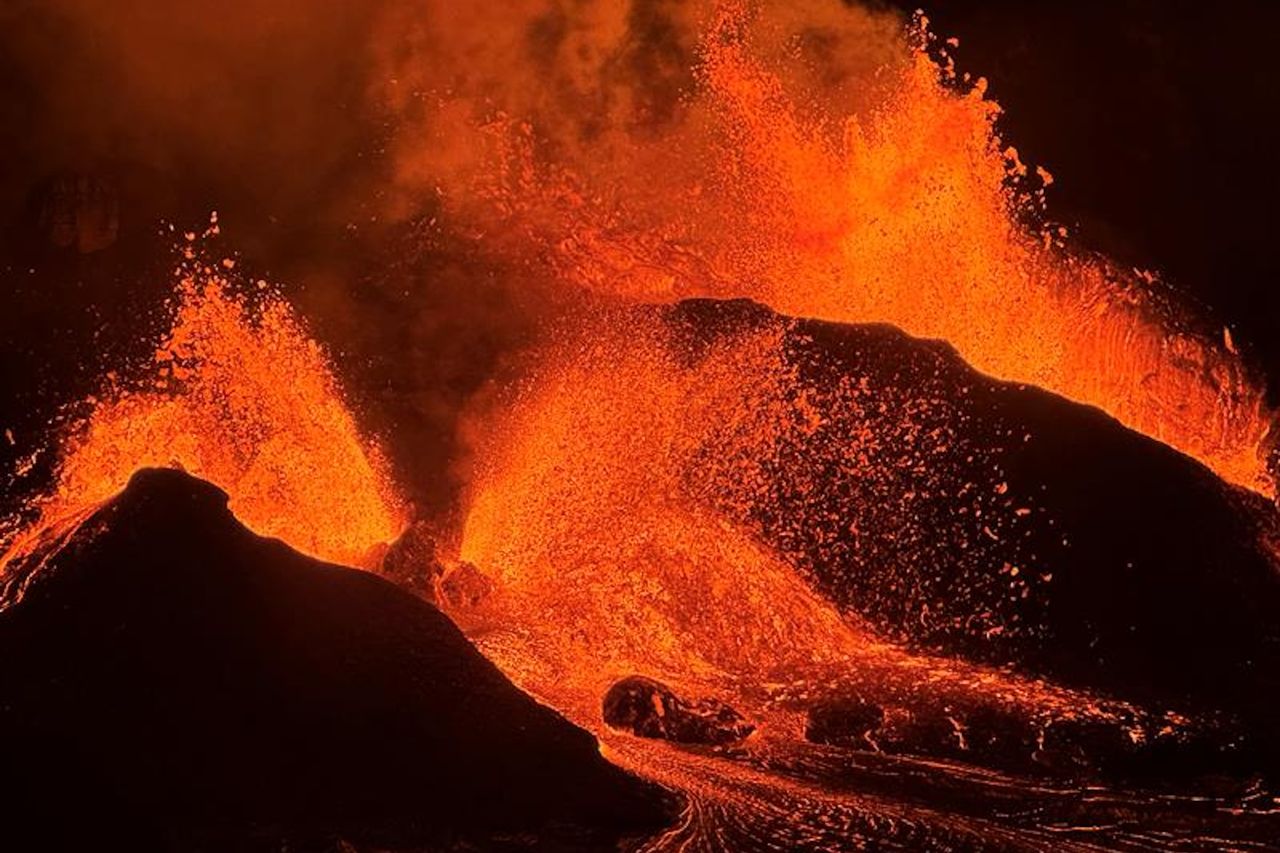 Glowing red lava splashes against dark, black rocks in a nighttime scene