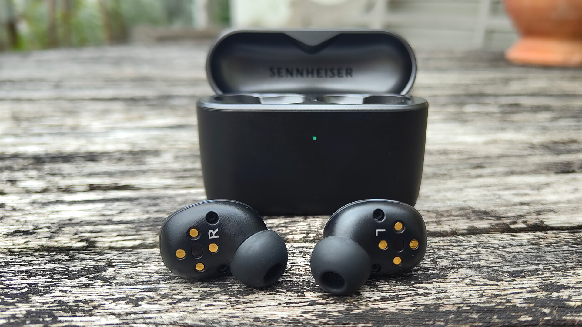 Sennheiser Momentum True Wireless 5 wireless earbuds next to case on wooden outdoor table