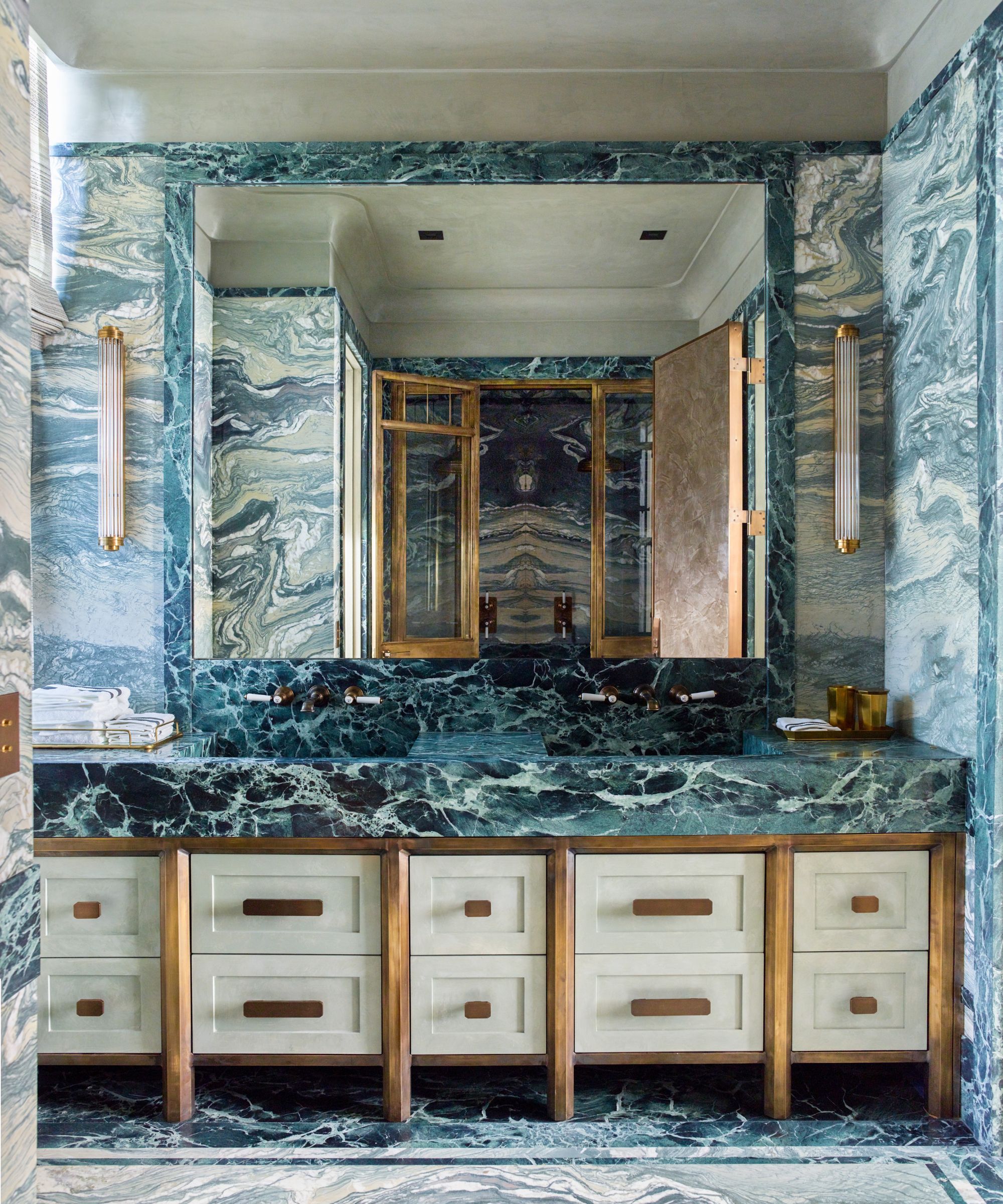 Dramatic bathroom featuring floor-to-ceiling teal veined marble, a matching double vanity, and a large inset mirror with vertical sconces.