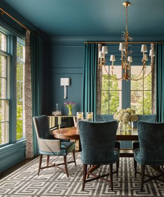 colors that go with teal, teal dining room with teal walls and ceiling, teal and patterned drapes, antique table, upholstered dining chairs, grey patterned rug, large brass and white chandelier with shades, mirrored console