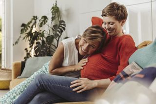 woman listening to the tummy of another pregnant woman with red highlights, one method of baby gender prediction