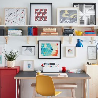 White room with colorful picture frames on a rack and a black top desk with a yellow chair