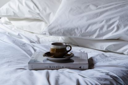 White sheets on bed and book and cup and saucer