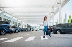 Young woman with luggage crossing at an airport zebra crossing