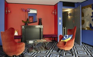 Hotel room with red and blue walls, patterned carpet and orange chairs