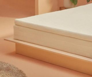 Corner of the Earthfoam Mattress Topper on a wooden bed base against peach-colored walls.