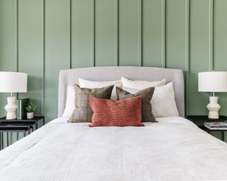 calming bedroom with sage green panelled wall, white bedding and earthy-colored cushions