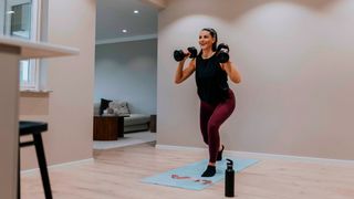 Woman performs a lunge while holding dumbbells in a home