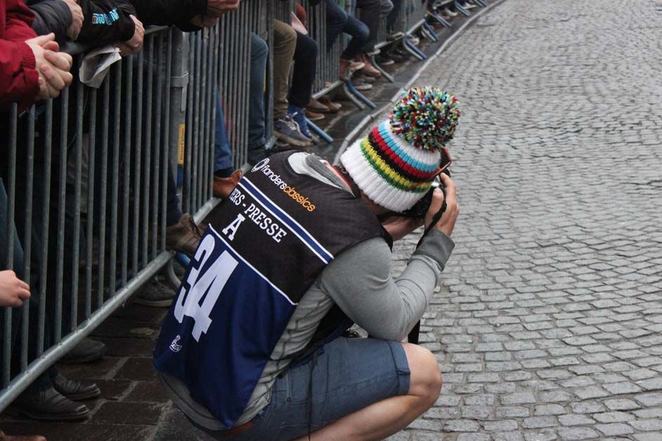 A photographer in a rainbow hat captures pictures of the riders at the start