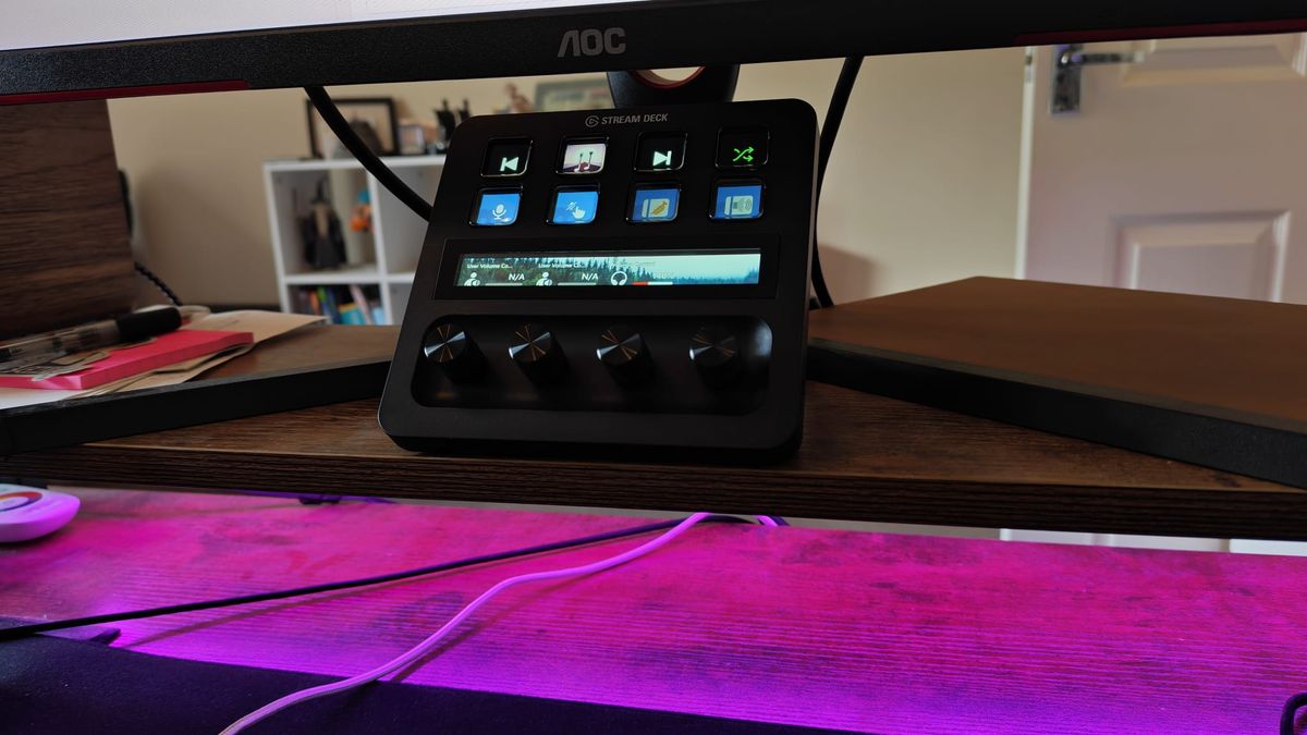 A Stream Deck Plus on a gaming desk above pink RGB lighting