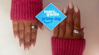 A woman's hand with pink nails and a pink sleeve wearing silver Oura Ring 4 on index finger with Tom's Guide Prime Day logo