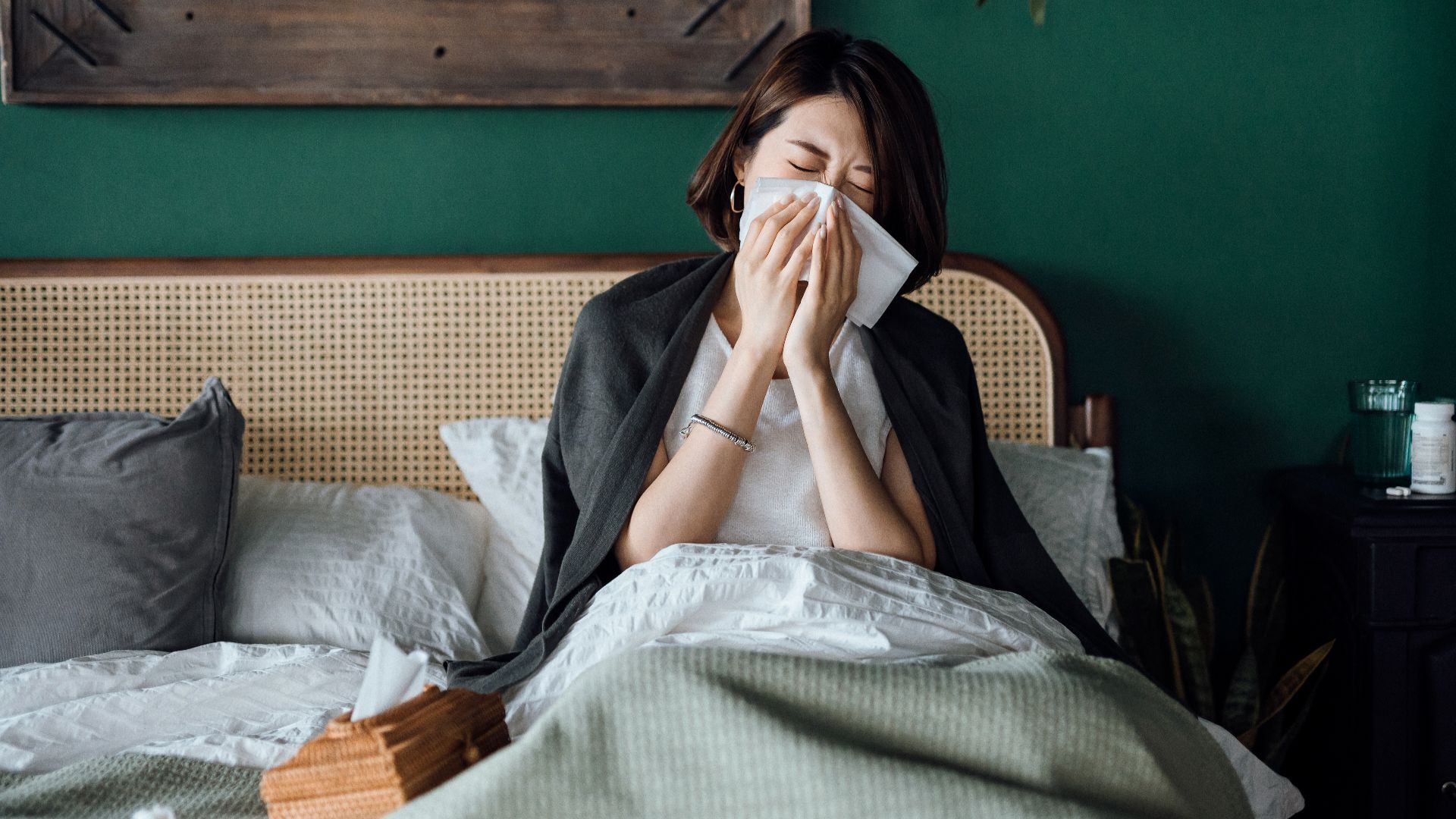 Woman sneezing while sitting in bed