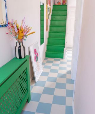 A small entryway with a green staircase and console table, pink walls, and a baby blue and white checkered floor